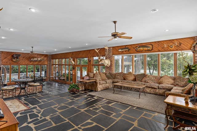 living room with ceiling fan, wood walls, and a healthy amount of sunlight