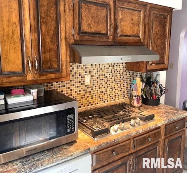 kitchen featuring stainless steel appliances, light stone counters, tasteful backsplash, and exhaust hood