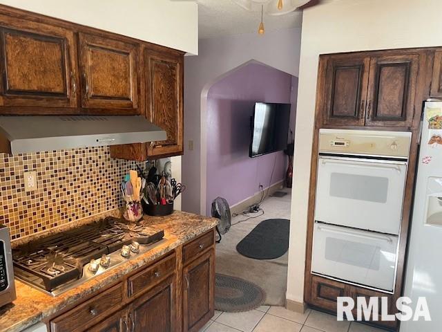 kitchen featuring light stone countertops, light tile patterned floors, range hood, tasteful backsplash, and stainless steel appliances