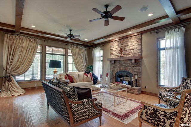 living room featuring ceiling fan, a stone fireplace, beamed ceiling, and light wood-type flooring