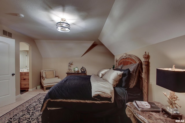 carpeted bedroom featuring ensuite bath and vaulted ceiling