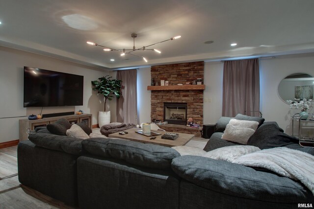 living room featuring a stone fireplace, an inviting chandelier, and light hardwood / wood-style flooring