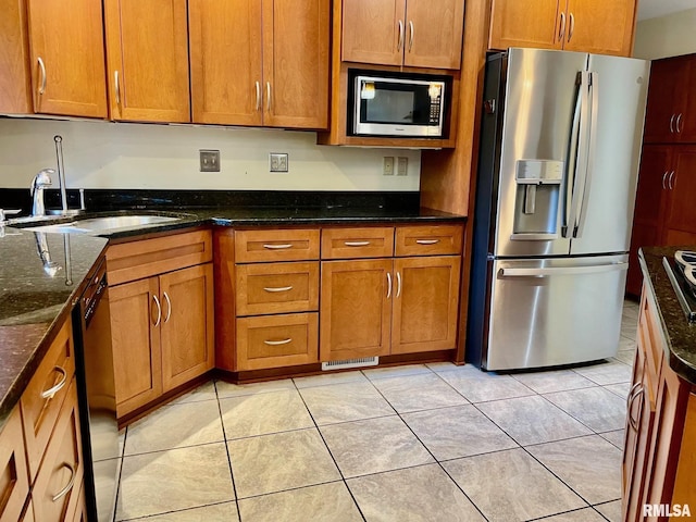 kitchen with light tile patterned flooring, stainless steel appliances, sink, and dark stone counters