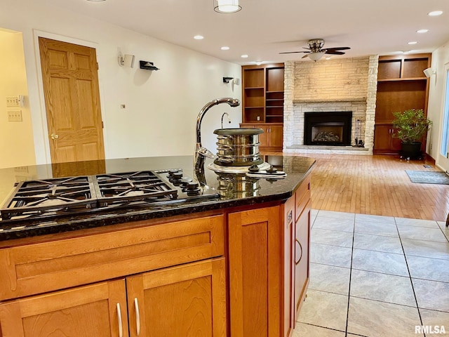 kitchen with built in shelves, a fireplace, light tile patterned floors, ceiling fan, and black gas cooktop