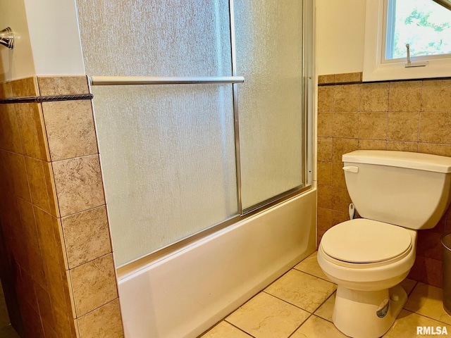 bathroom with tile walls, combined bath / shower with glass door, tile patterned floors, and toilet