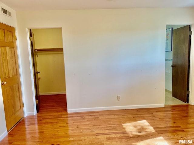 unfurnished bedroom featuring a walk in closet, a closet, and light wood-type flooring