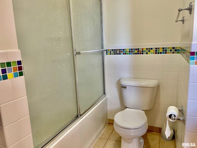 bathroom with tile patterned flooring, combined bath / shower with glass door, tile walls, and toilet