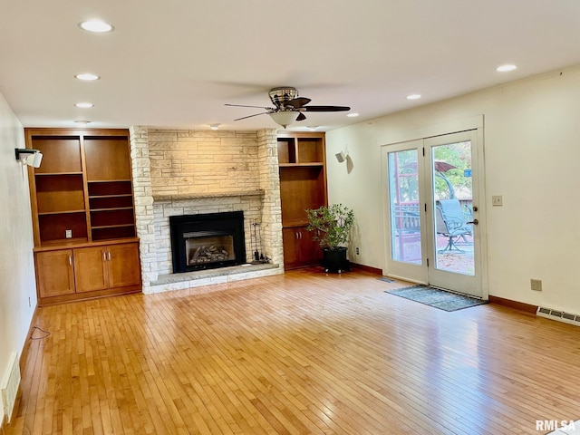 unfurnished living room with ceiling fan, a stone fireplace, light hardwood / wood-style flooring, and built in features