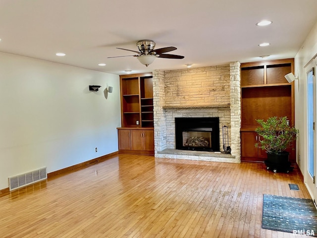 unfurnished living room featuring wood-type flooring, a stone fireplace, built in features, and ceiling fan