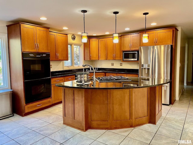 kitchen featuring an island with sink, appliances with stainless steel finishes, dark stone countertops, and decorative light fixtures