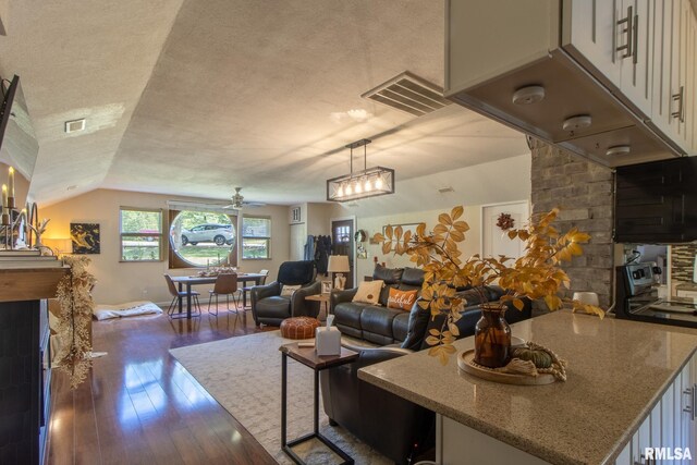 kitchen featuring a textured ceiling, dark hardwood / wood-style floors, vaulted ceiling, hanging light fixtures, and stone counters