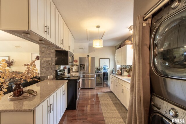 kitchen featuring pendant lighting, stainless steel appliances, white cabinets, and stacked washer / dryer