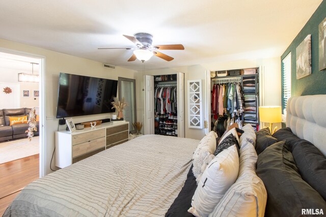 bedroom featuring two closets, hardwood / wood-style floors, and ceiling fan