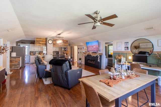 dining area featuring ceiling fan, vaulted ceiling, a fireplace, and dark hardwood / wood-style flooring