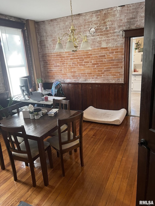 dining room featuring brick wall, a notable chandelier, wainscoting, and hardwood / wood-style flooring