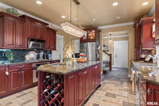 kitchen featuring hanging light fixtures, sink, a center island with sink, stainless steel appliances, and dark stone counters