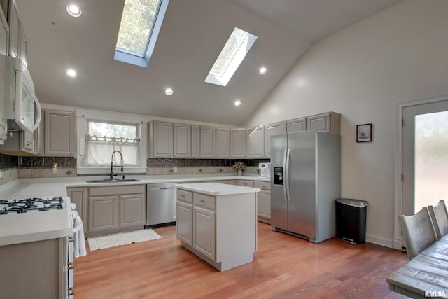 kitchen featuring sink, high vaulted ceiling, appliances with stainless steel finishes, a center island, and light wood-type flooring