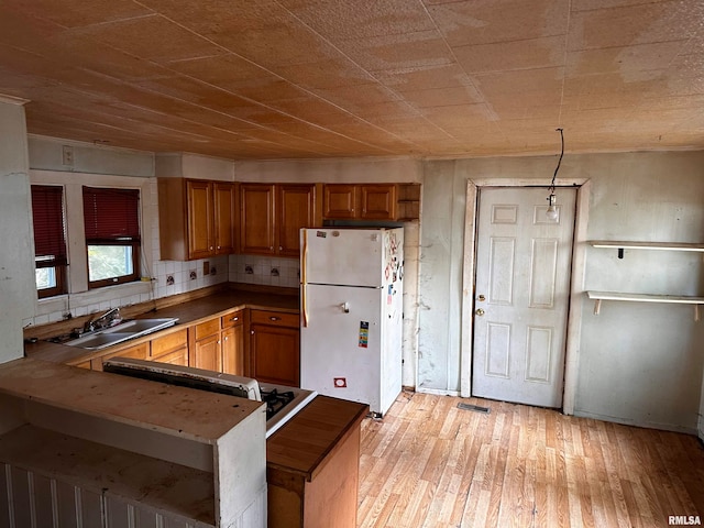 kitchen with backsplash, kitchen peninsula, white fridge, light hardwood / wood-style flooring, and sink