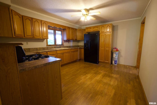 kitchen featuring light wood-type flooring, a textured ceiling, sink, black appliances, and crown molding