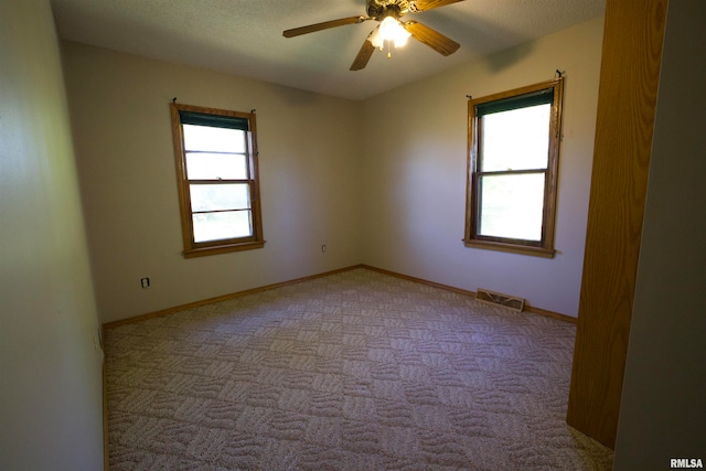 unfurnished room featuring a textured ceiling, ceiling fan, light carpet, and a wealth of natural light