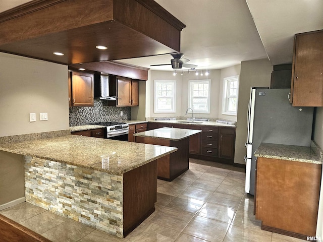 kitchen featuring light stone counters, sink, kitchen peninsula, wall chimney range hood, and stainless steel appliances