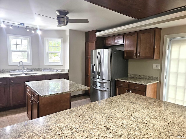 kitchen with ceiling fan, sink, stainless steel refrigerator with ice dispenser, a center island, and light stone countertops