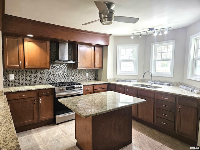 kitchen featuring sink, stainless steel range with gas stovetop, wall chimney range hood, backsplash, and light stone countertops