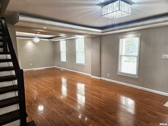 empty room featuring hardwood / wood-style floors, ornamental molding, an inviting chandelier, and a raised ceiling