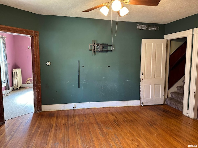 unfurnished room featuring ceiling fan, radiator, hardwood / wood-style flooring, and a textured ceiling