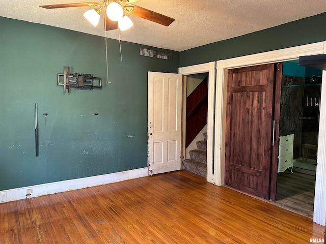 unfurnished bedroom featuring wood-type flooring, a textured ceiling, a closet, and ceiling fan