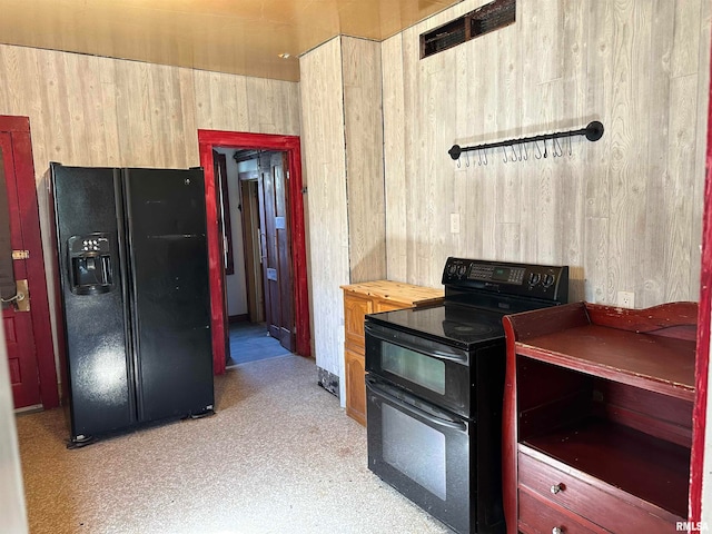 kitchen featuring black appliances, wood walls, and light brown cabinetry