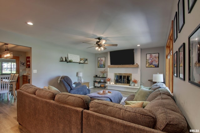 living room featuring ceiling fan, a large fireplace, and light hardwood / wood-style floors