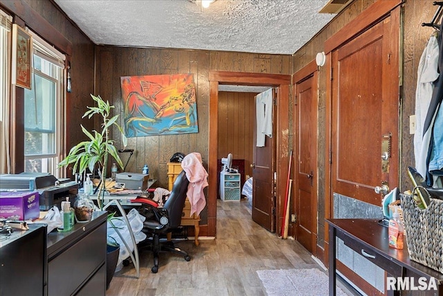 office space with a textured ceiling, light wood-type flooring, and wooden walls