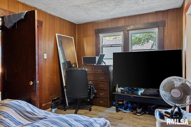 bedroom with a textured ceiling, wooden walls, and light hardwood / wood-style flooring