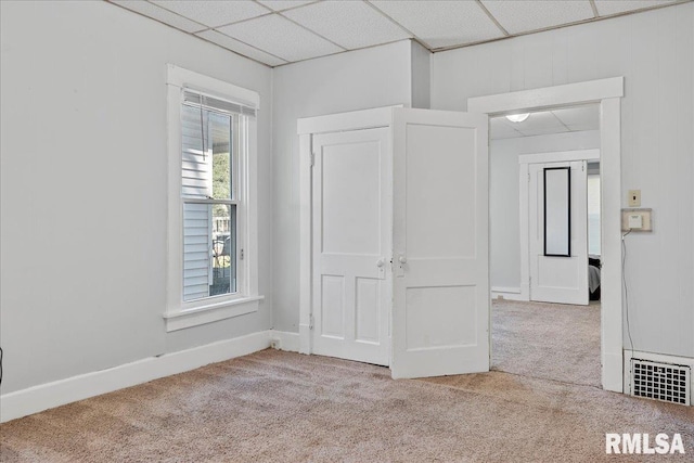 unfurnished bedroom featuring light carpet, a paneled ceiling, and a closet