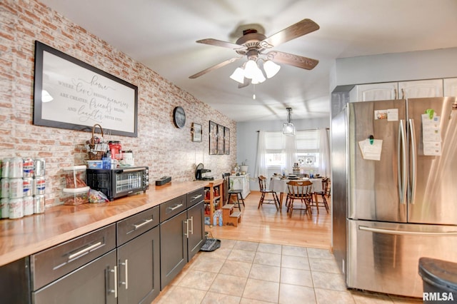 kitchen with stainless steel fridge, light wood-type flooring, ceiling fan, and brick wall