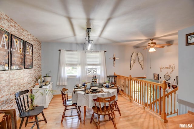 dining space featuring brick wall, light hardwood / wood-style flooring, and ceiling fan