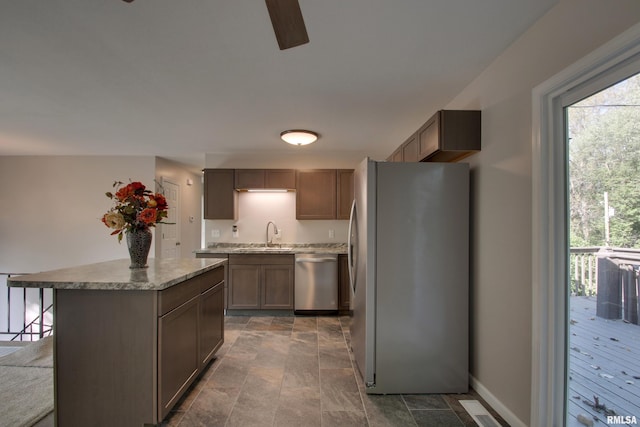 kitchen with ceiling fan, sink, stainless steel appliances, light stone countertops, and a center island