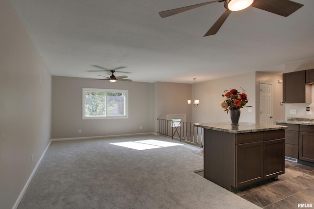 kitchen with light stone counters, dark colored carpet, ceiling fan with notable chandelier, hanging light fixtures, and dark brown cabinets