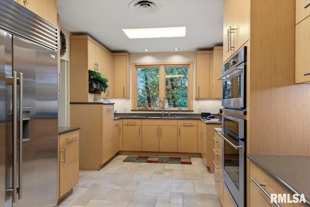 kitchen featuring built in refrigerator, light brown cabinetry, and sink