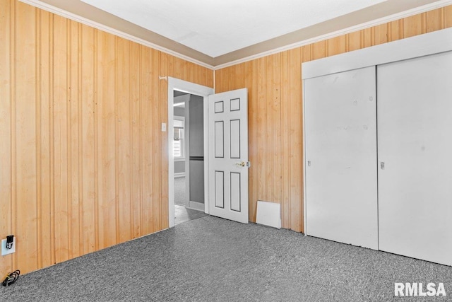 unfurnished bedroom with crown molding, wooden walls, a closet, and carpet flooring