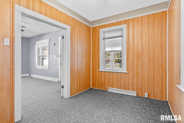 empty room with dark colored carpet, wooden walls, a textured ceiling, and baseboard heating