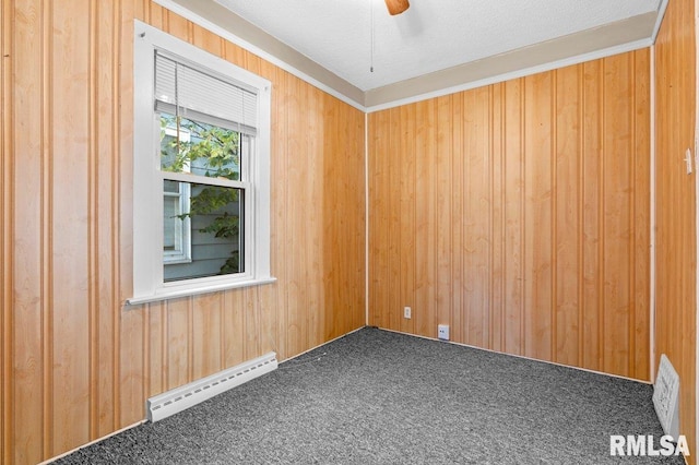 carpeted empty room featuring ceiling fan, a textured ceiling, baseboard heating, and wood walls