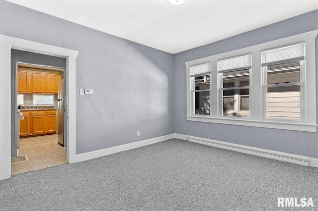 unfurnished room featuring a healthy amount of sunlight, a baseboard heating unit, light carpet, and a textured ceiling