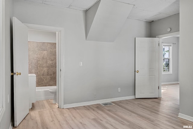 unfurnished bedroom with a drop ceiling, ensuite bathroom, and light wood-type flooring