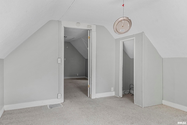 additional living space with a textured ceiling, vaulted ceiling, and light colored carpet