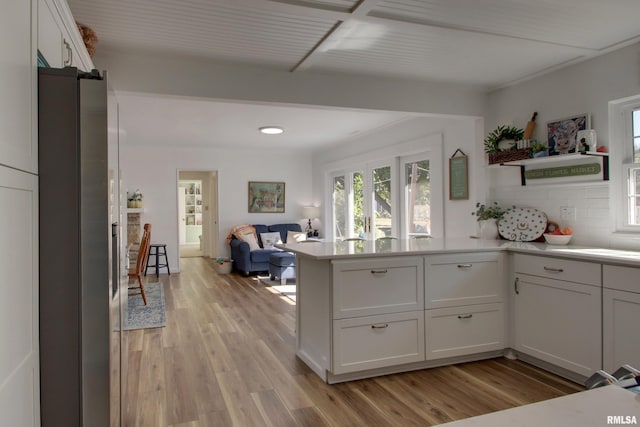 kitchen with light hardwood / wood-style floors, decorative backsplash, white cabinetry, and kitchen peninsula