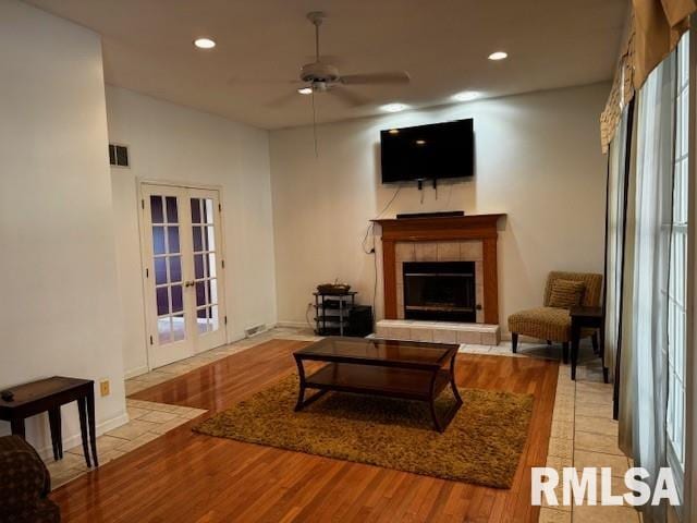 living room with a tile fireplace, ceiling fan, french doors, and light wood-type flooring