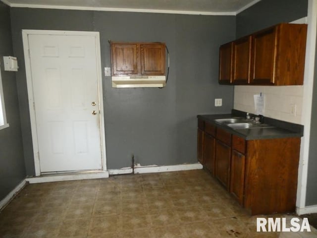 kitchen with tasteful backsplash, baseboards, dark countertops, under cabinet range hood, and a sink