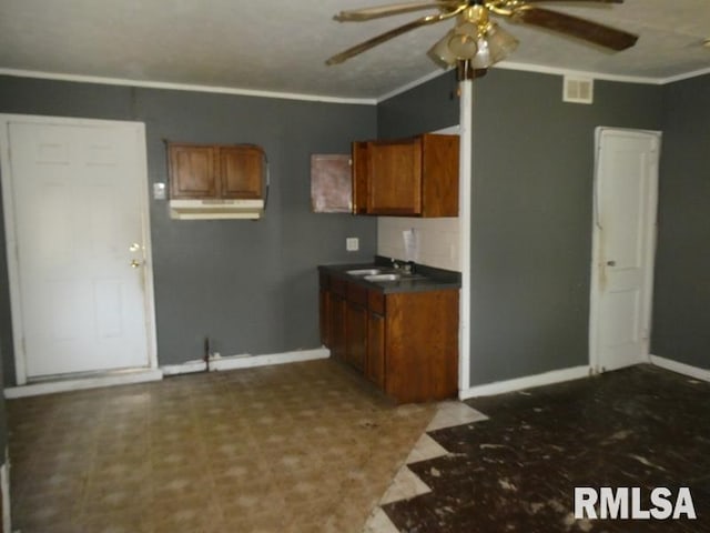 kitchen featuring dark countertops, ornamental molding, brown cabinetry, and a sink